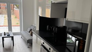 Cozinha moderna com bancada preta, eletrodomésticos de aço inoxidável e um sofá cinza na área de estar vizinha.