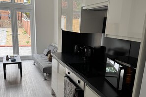 A modern kitchen with a black countertop, stainless steel appliances, and a grey sofa in the adjacent living area. - Modern 2-bed Apartment Sleeps 5 Fast Links Central (London)