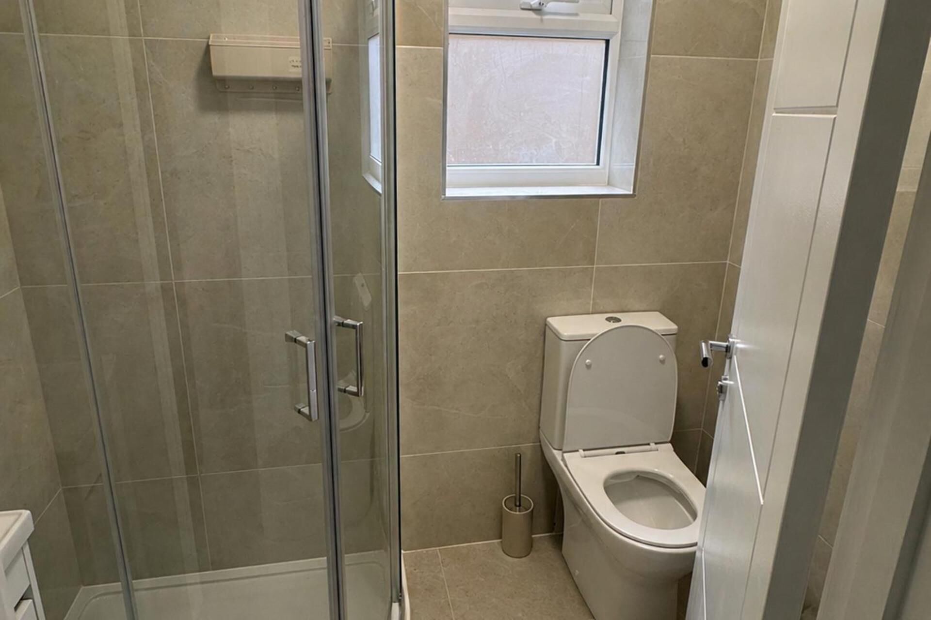 A bathroom with a glass shower enclosure, a toilet, and a window above the toilet.