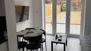 Uma sala de estar moderna com área de jantar, grandes portas de vidro deslizantes para um quintal e uma TV de tela plana fixada na parede.