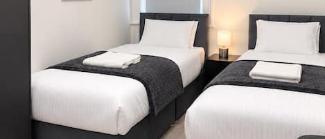 Una habitación de hotel con dos camas, un armario, una mesita de noche con lámpara y una ventana con persianas.
