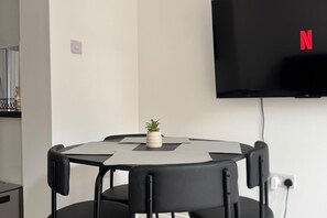 A round table with four chairs, a small potted plant, and a flat-screen TV mounted on the wall. - Modern 2-bed Apartment Sleeps 5 Fast Links Central (London)
