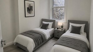 Quarto com duas camas, uma mesa de cabeceira, um abajur e um quadro na parede.