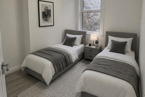 A bedroom with two beds, a nightstand, a lamp, and a framed picture on the wall. - Modern 2-bed Apartment Sleeps 5 Fast Links Central (London)