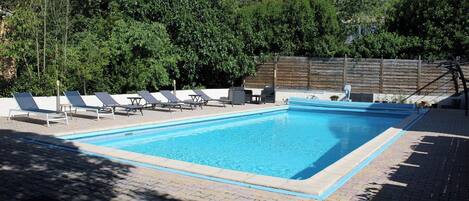 Piscina rectangular con borde de azulejos, rodeada de sillas de descanso y una valla de madera.