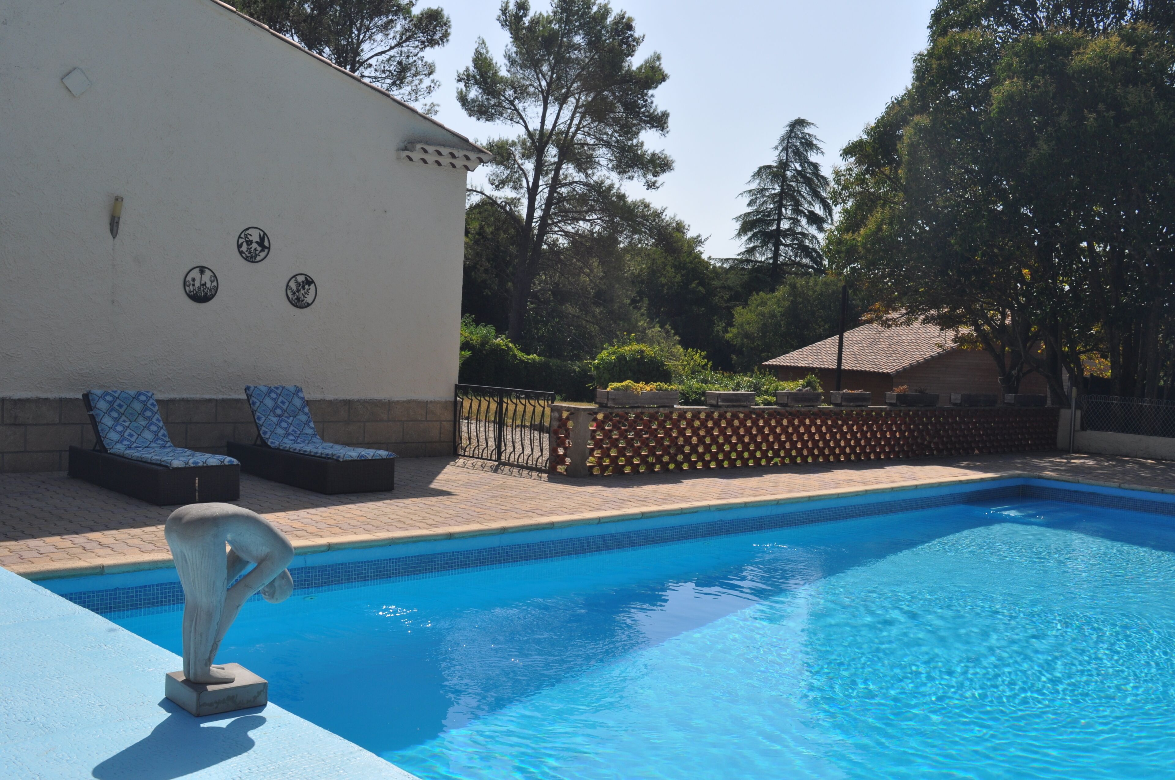 Una piscina con lettini, una scultura decorativa e un muro con motivi circolari.