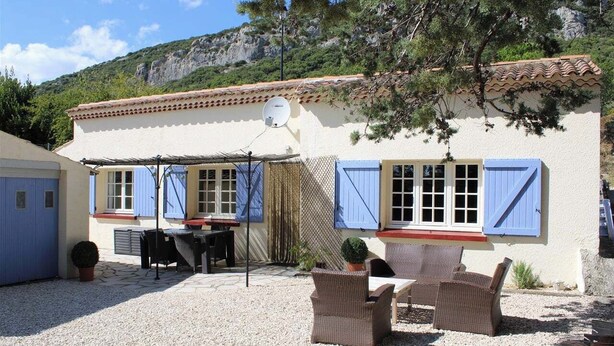 Un edificio con fachada blanca, contraventanas azules y un patio con muebles de mimbre.