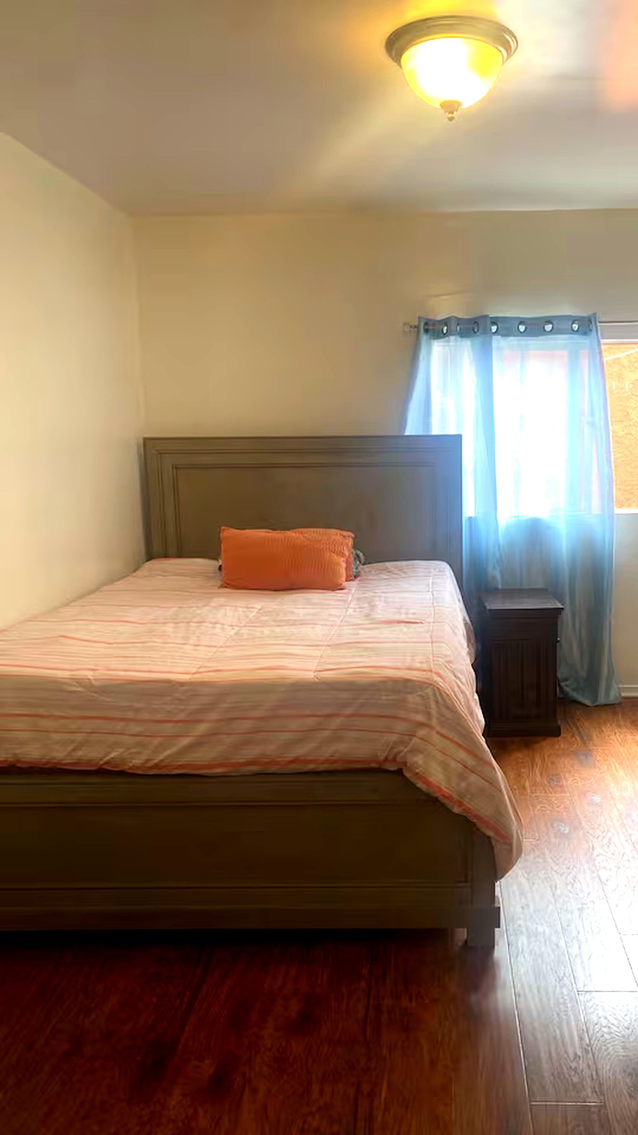 A bedroom with a bed, a nightstand, a window with curtains, and a ceiling light.