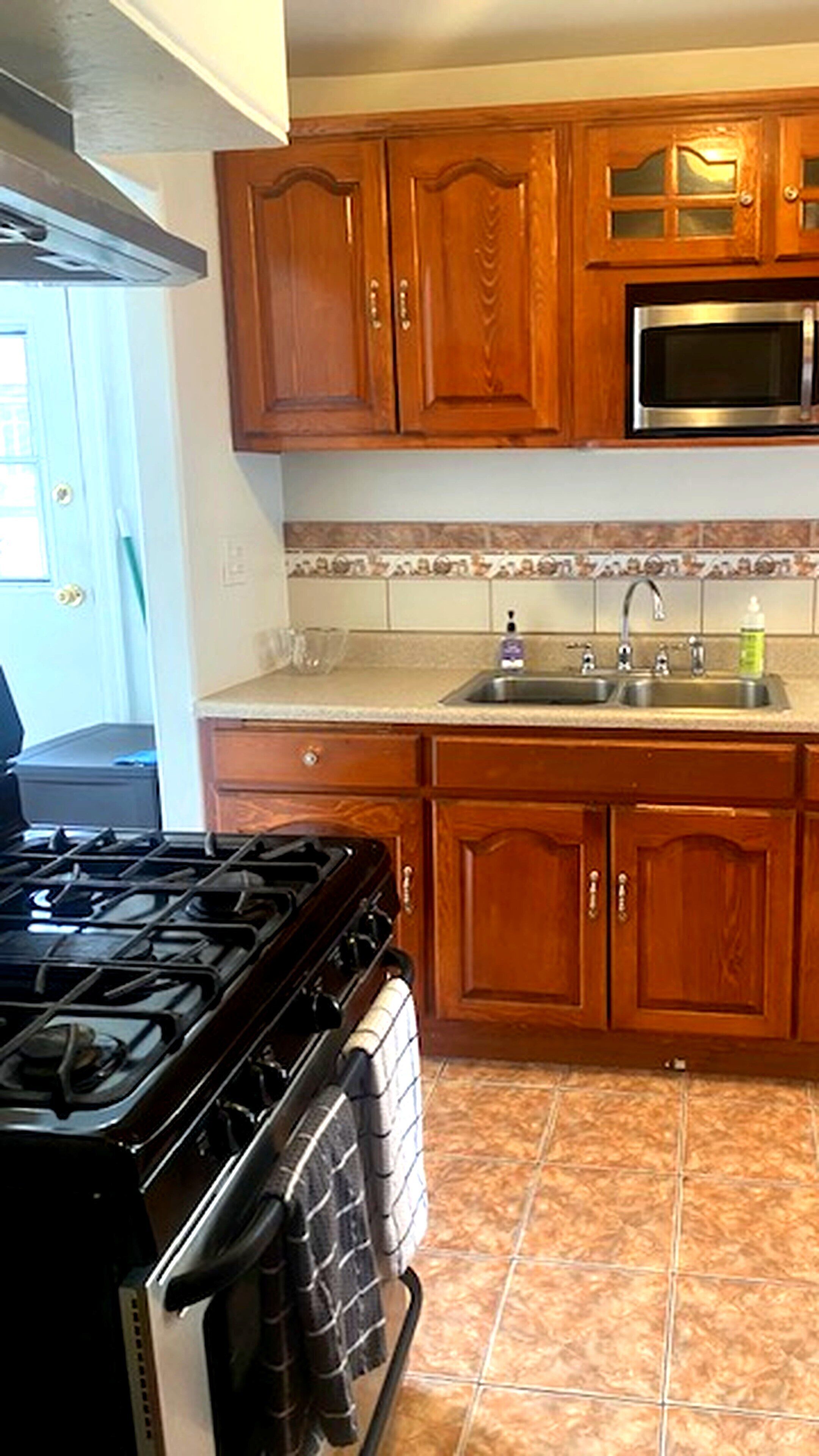 A kitchen with wooden cabinets, a stainless steel sink, a microwave, and a stove.