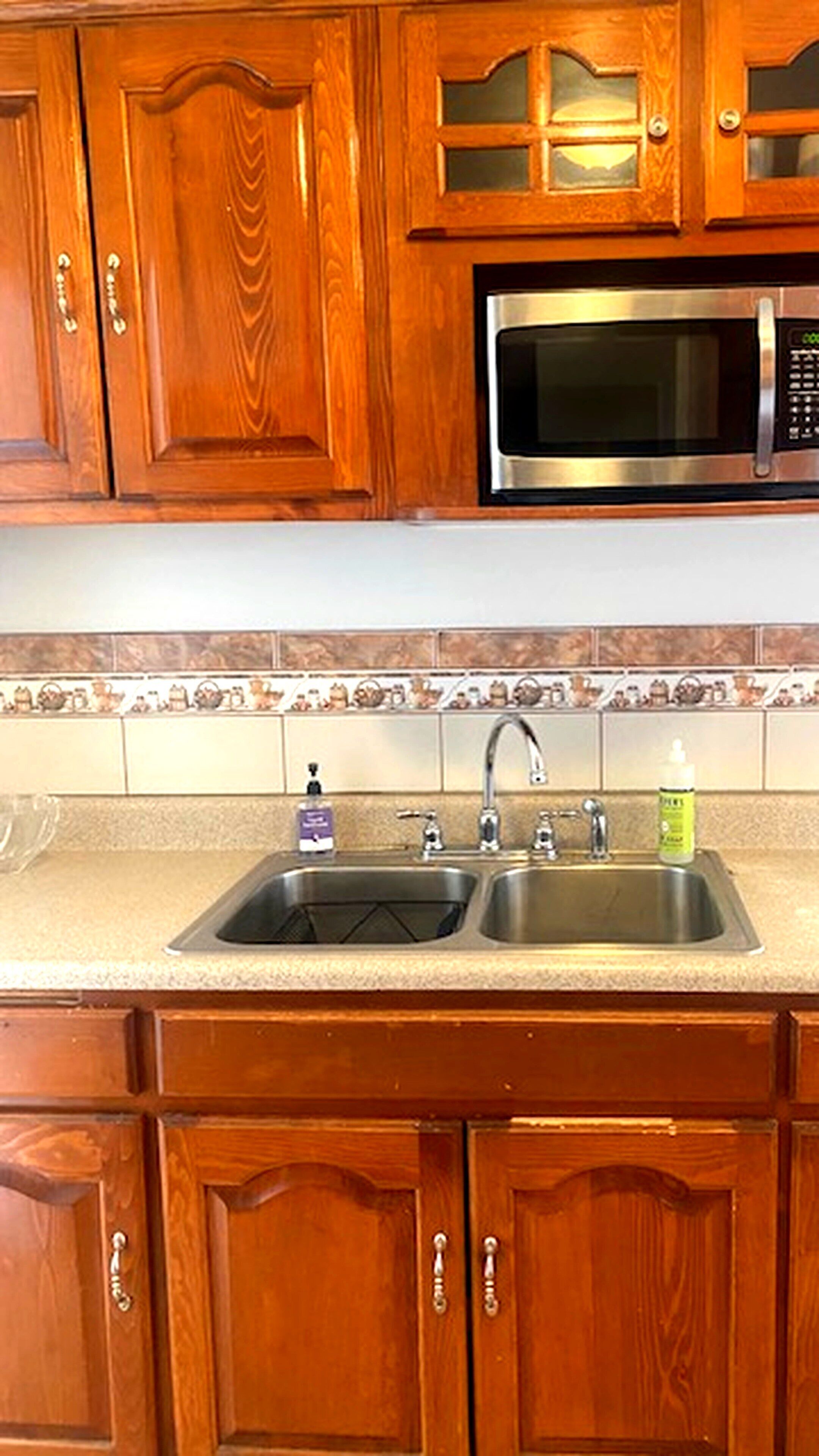 A kitchen with wooden cabinets, a stainless steel sink, and a microwave.