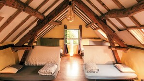 A room with two single beds, wooden beams, a hanging light fixture, and a window with a view.