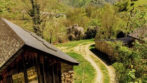 A rustic wooden building with a sloped roof, surrounded by a dirt path and lush greenery.