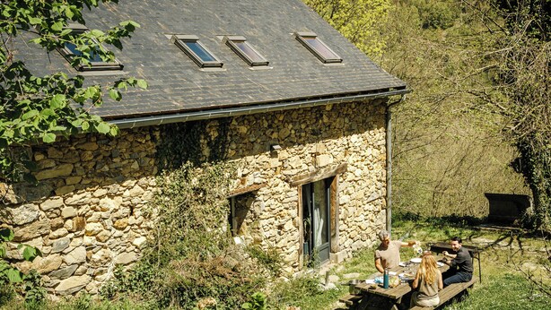 A stone building with a sloped roof and skylights, a wooden deck, and a stone wall.