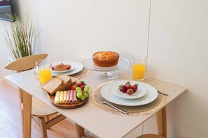 Ein Frühstückstisch mit einer Platte Schinken, Käse und Trauben, einer Scheibe Brot, einem Muffin und einem Glas Orangensaft.