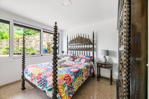 Een hemelbed met een bloemenbedekking, een nachtkastje met een lamp, en uitzicht op groen buiten.