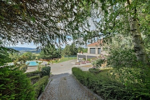 A paved pathway leading to a pool, surrounded by lush greenery and a building with a red roof. - Room “La Chambre Tom” with Shared Pool, Communal Garden and Wi-Fi (Saint-Victor)