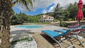 Une piscine entourée de chaises longues, avec une maison en arrière-plan.