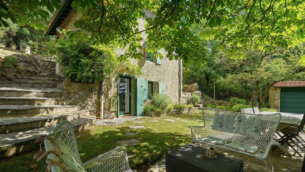 A stone building with a green door, outdoor seating, and a stone staircase.