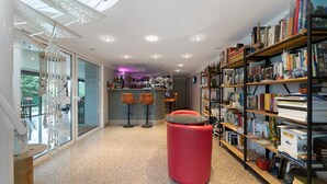 A modern interior with a bar area, bookshelves, and a red ottoman.