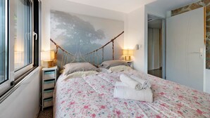 A bedroom with a bed, two bedside tables, a window, a wall-mounted lamp, and a door.