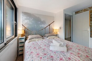 Una camera da letto con un letto, due comodini, una finestra, una lampada a parete e una porta.