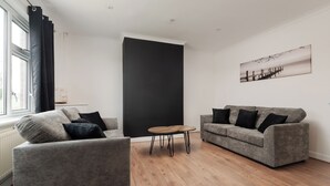 Una sala de estar moderna con dos sofás grises, una mesita de centro de madera y una pared de acento negra grande.