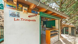 Ein rustikales Straßencafé mit Holztresen, einer grünen Markise und verschiedenen Schildern, darunter 'La Trinquette'.