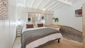 Ein Schlafzimmer mit einem Bett, Nachttischen, einem Spiegel, einem großen Felsen und einer Zimmerpflanze.