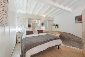 A bedroom with a bed, bedside tables, a mirror, a large rock, and a potted plant.