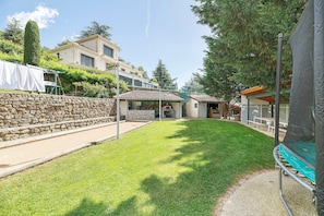 A residential property with a stone wall, a grassy lawn, and a covered patio area. - Chalet "Au Domaine De Cabu" with Mountain View, Shared Pool and Wi-Fi (Saint-Victor)