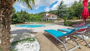 Ein Poolbereich mit Liegestühlen, einem roten Sonnenschirm und einem Haus im Hintergrund.
