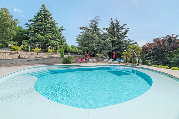 A swimming pool with a curved edge, surrounded by trees and a seating area with umbrellas.