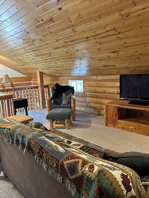 Ein Holzblockhaus-Interieur mit einer gemütlichen Sitzecke, einem Fernseher und einem Fenster.