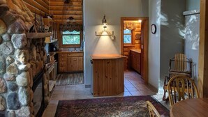 A log cabin interior with a stone wall, wooden cabinets, a central island, and a dining area with chairs. - Cozy lake cabin in Crosslake with a fireplace, perfect for relaxing getaways. (Crosslake)