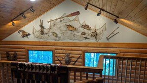 A log cabin interior with a ceiling decorated with fishing nets and fish, a large window, and a wooden bench. - Cozy lake cabin in Crosslake with a fireplace, perfect for relaxing getaways. (Crosslake)