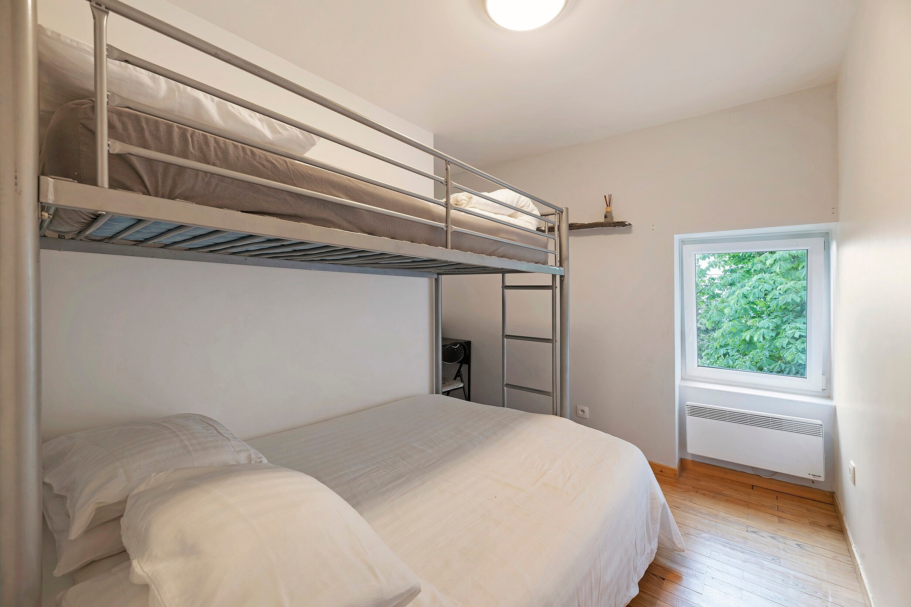 A bunk bed room with a window, a radiator, and a wooden floor.