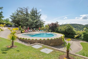 Una piscina circular con sillas de descanso y un muro de piedra, rodeada de follaje y árboles.