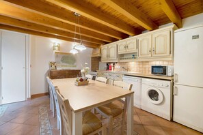 A kitchen with wooden beams, a washing machine, a microwave, and a dining area with chairs and a table. - Holiday Home 'Bergerie at Domaine de Cabu' with Mountain View, Shared Pool and Wi-Fi (Saint-Victor)