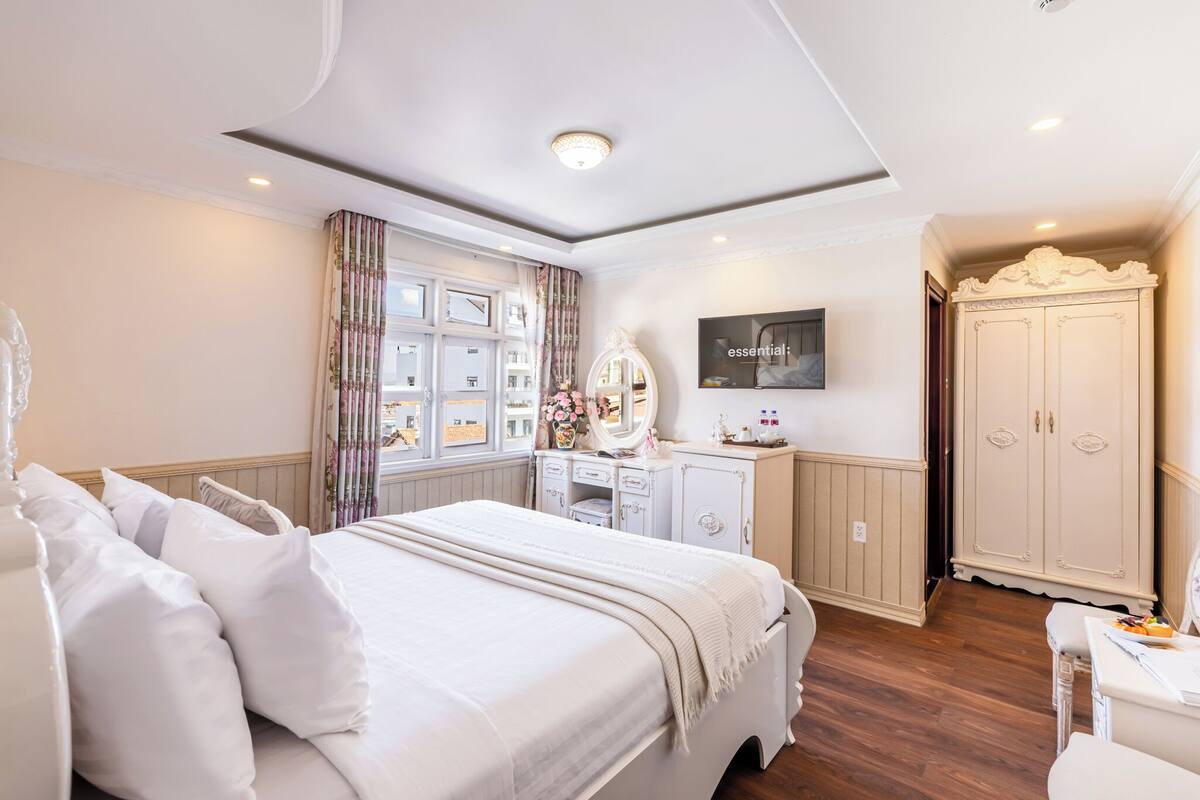 A bedroom with a large bed, a vanity with a mirror, a wardrobe, and a television on the wall.
