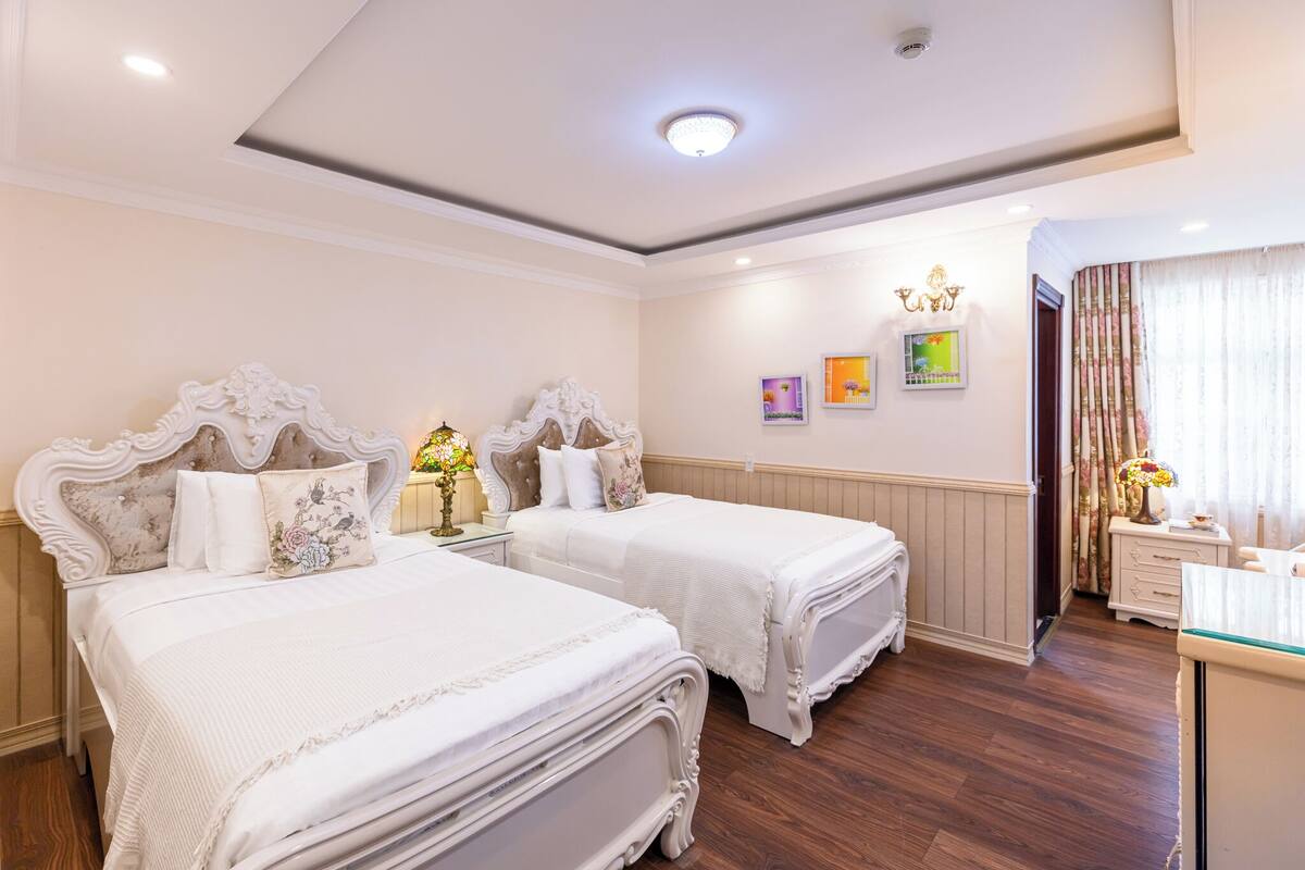 A hotel room with two beds, a desk, a mirror, a nightstand, and a window with curtains.