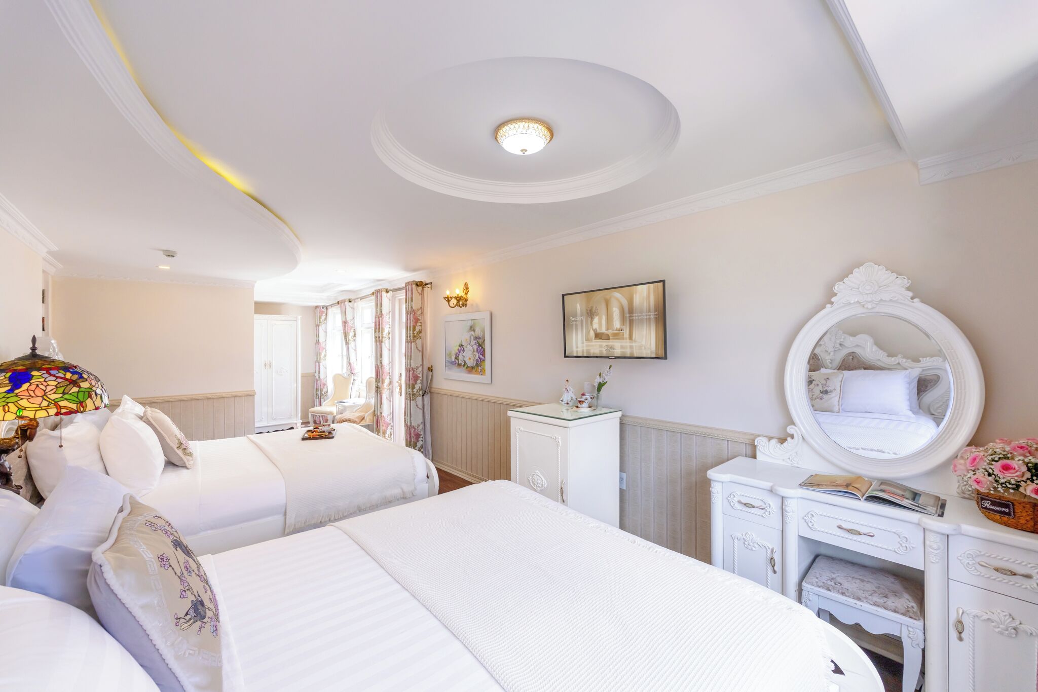 A hotel room with two beds, a white dresser, a mirror, and a chandelier.