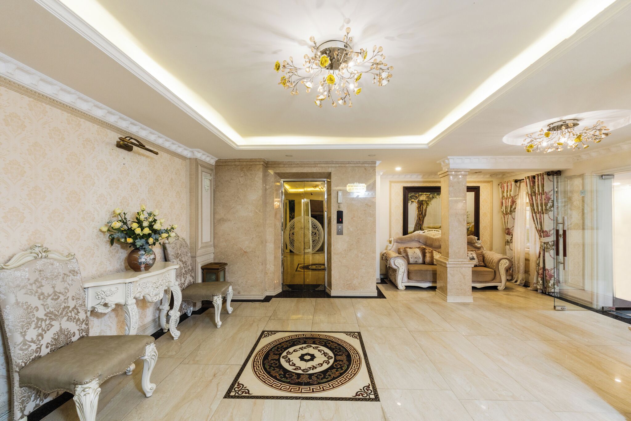Un hall d’entrée luxueux, avec un sol en marbre, des meubles richement décorés, un lustre et un tapis à motifs.