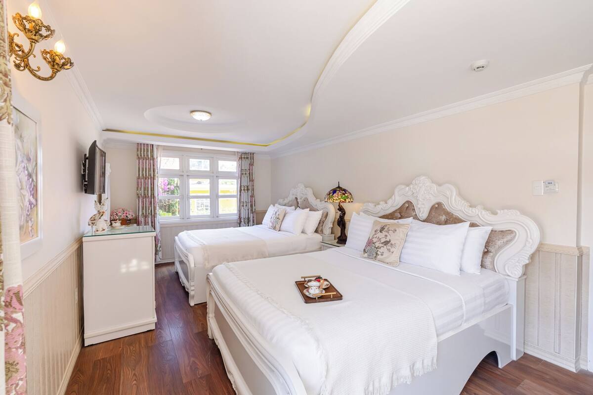 A hotel room with two beds, a TV, a small table, and a window with curtains.
