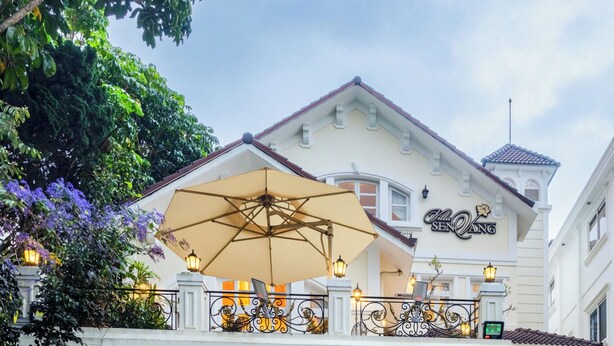 A hotel with a balcony, potted plants, and a well-lit entrance. - Hoa Sen Vang (Xuan Huong - Da Lat)