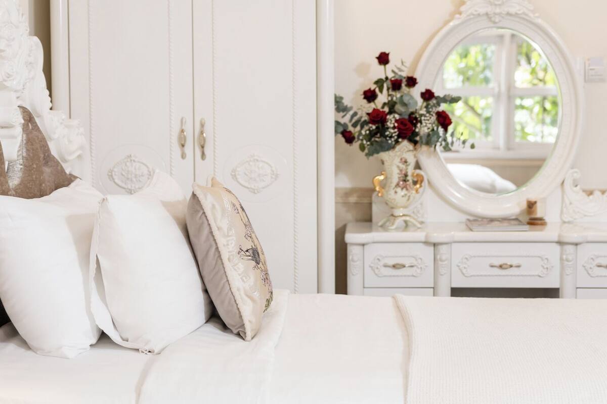 A bedroom with a white bed, a dresser with a mirror, and a large wardrobe.