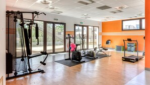 Una palestra con attrezzature per esercizi, ampie finestre e una parete arancione.