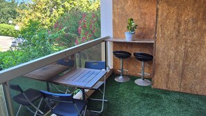 Een balkon met een tafel, stoelen, een klein krukje, een bloempot en een houten kast.