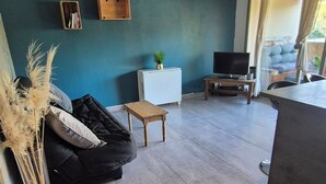 Een woonkamer met een donkere bank, een klein houten tafeltje, een televisie en een raam met gordijnen.