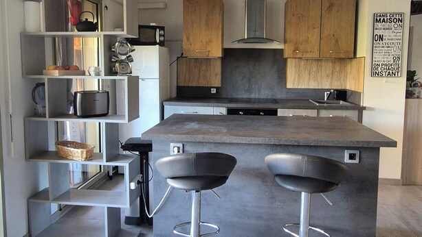 Een moderne keuken met een centraal kookeiland, twee barkrukken en houten keukenkastjes.