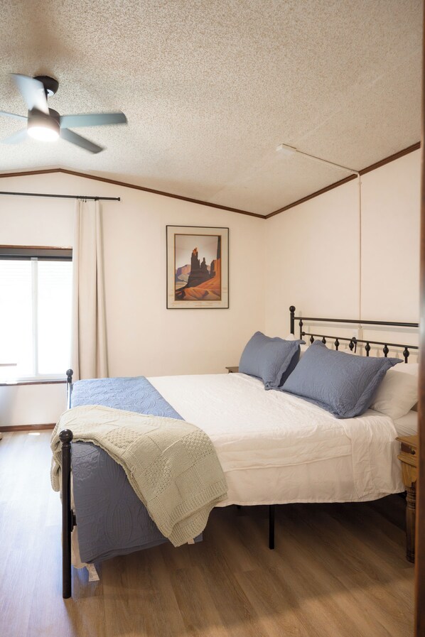 A bedroom with a bed, a ceiling fan, a window, and a painting on the wall. - Winchester KS Farmhouse Near KC - 3BR Country Home (Winchester)